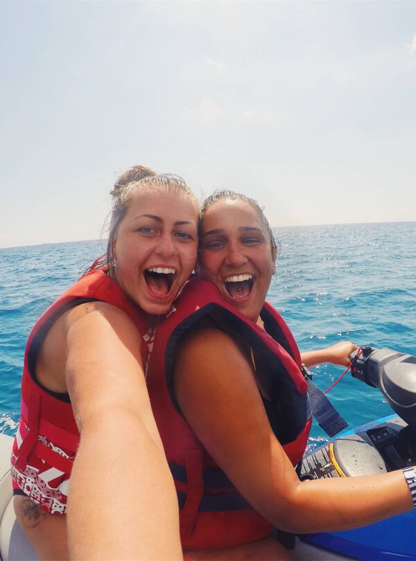 Tourists enjoying watersports in Bali, including jet skiing, parasailing, and banana boat rides against a backdrop of clear blue water and a sunny sky